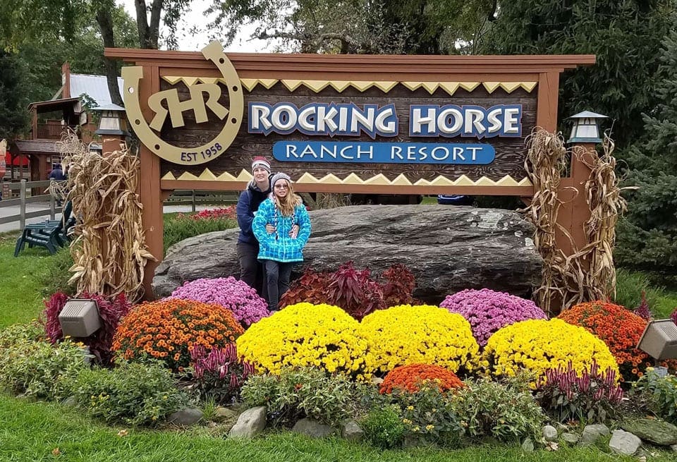 Mom and daughter stand togeether in front of the Rocking Horse Ranch Resort sign, one of the best summer lake resorts in the Northeast for families.
