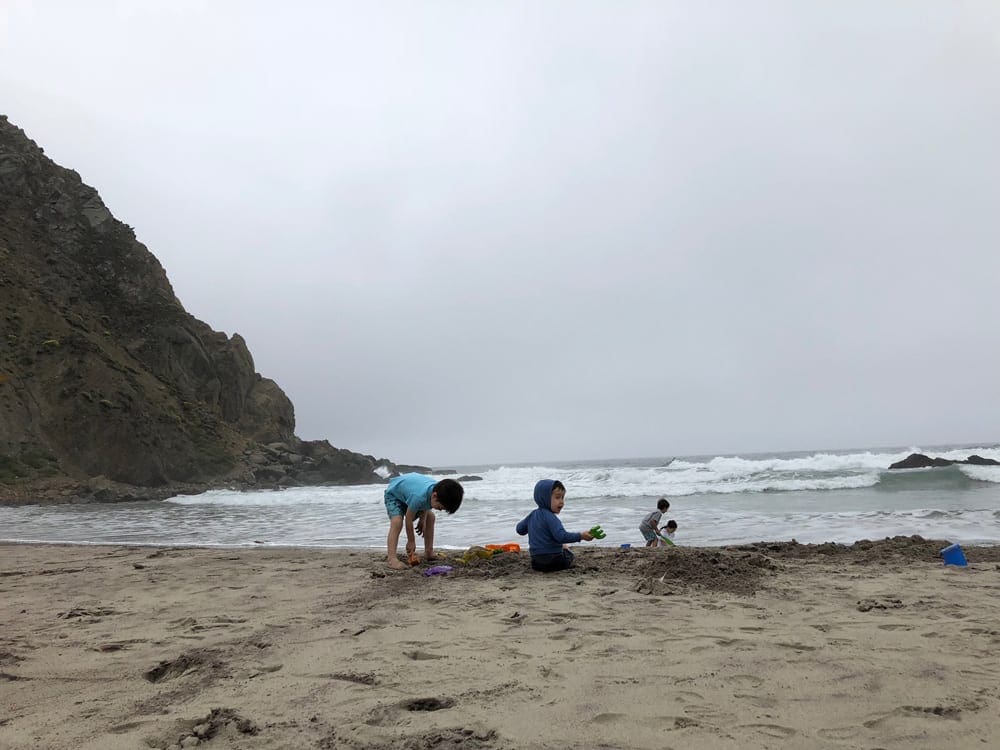Three kids play in the sand on a beach near Big Sur.