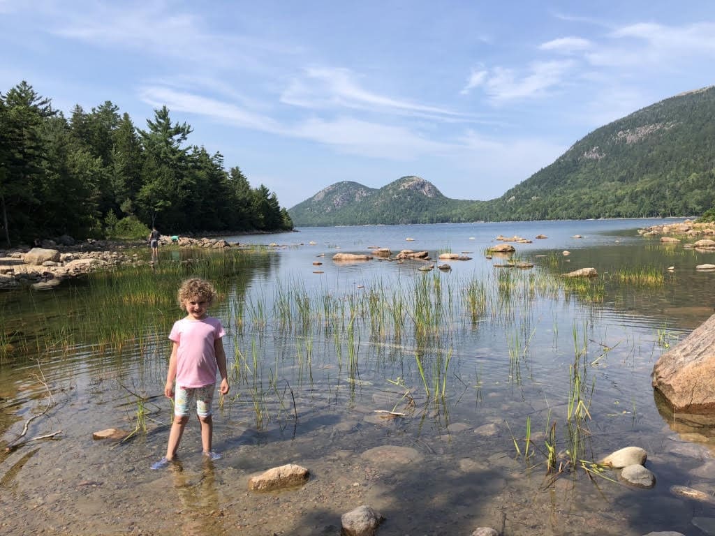 A young girl stands within a shallow lake in Maine.