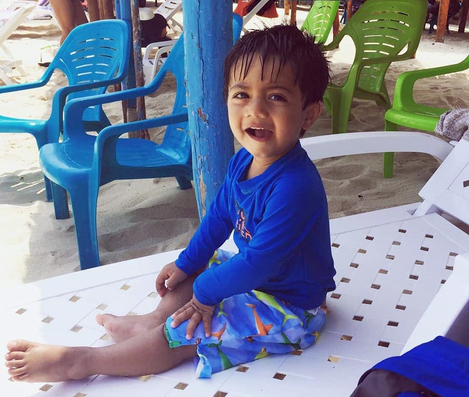 A young boy wearing a blue swimming suit smiles while sitting on a beach loungers in Isla Baru.