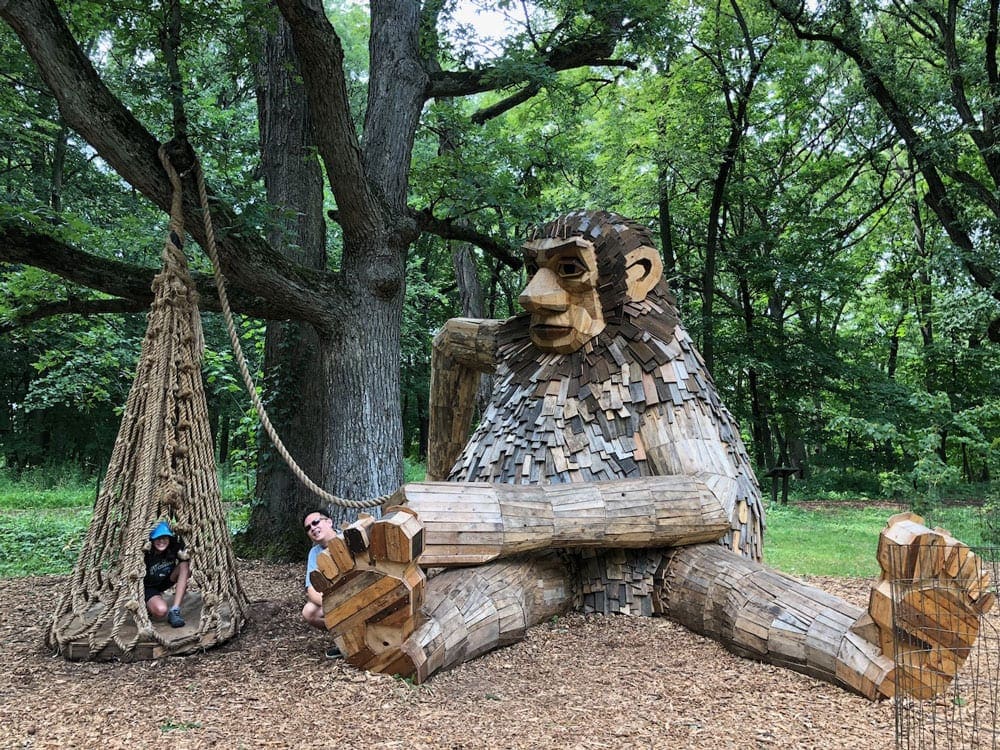 A young child explore a park with a huge wooden troll at the Morton Arboretum.