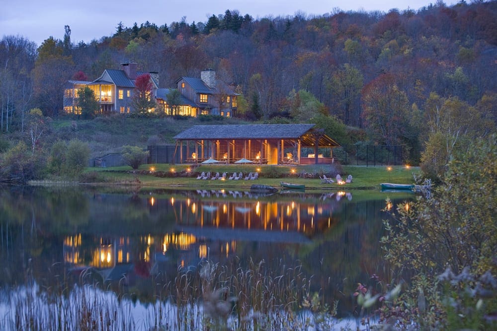 The rustic and charming buildings of the Twin Farms across a still body of water.