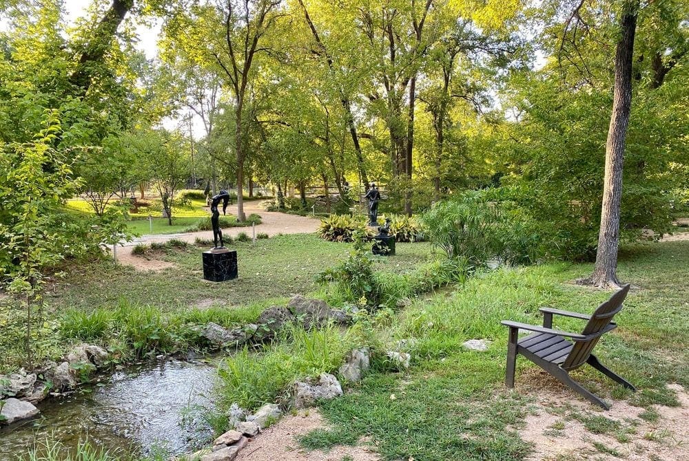 A view of a stream surrounded by statues at the UMLAUF Sculpture Garden Museum.