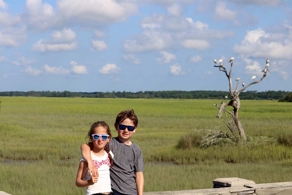 Brother and sister stand togehter with Kiawah Island extending behind them, one of the best islands in South Carolina for families.