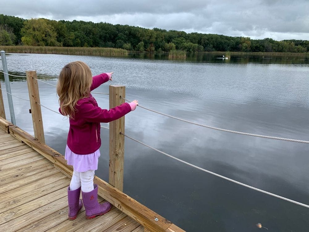 A young girl points across a pond at a bird while hiking along a boardwalk at Wood Lake Nature Center, one of the best things to do in Minneapolis with kids.
