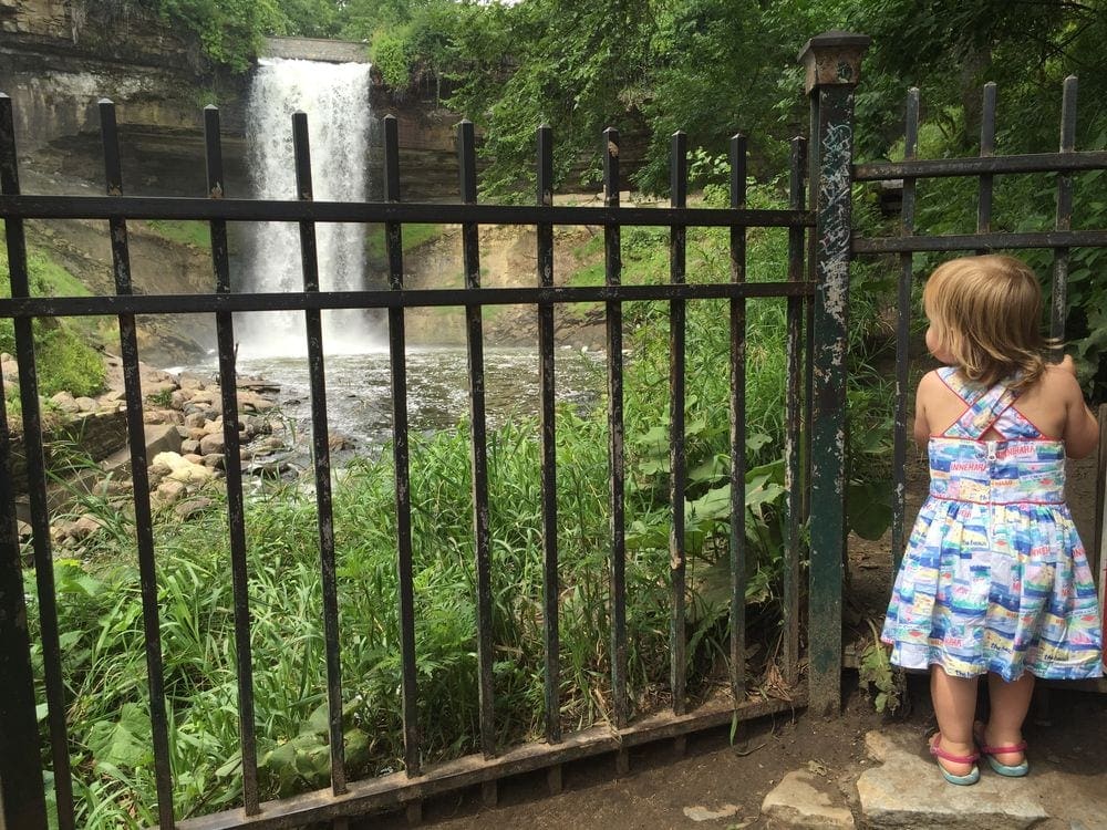 A young girl holds onto the railing while she peer at Minnehaha Falls in Minneapolis.