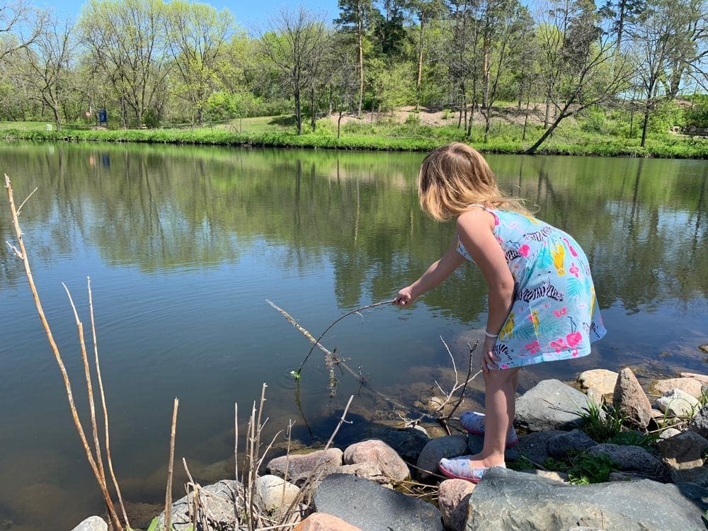 A young girl pokes a stick in the water on a sunny day in Northfield, Minnesota.