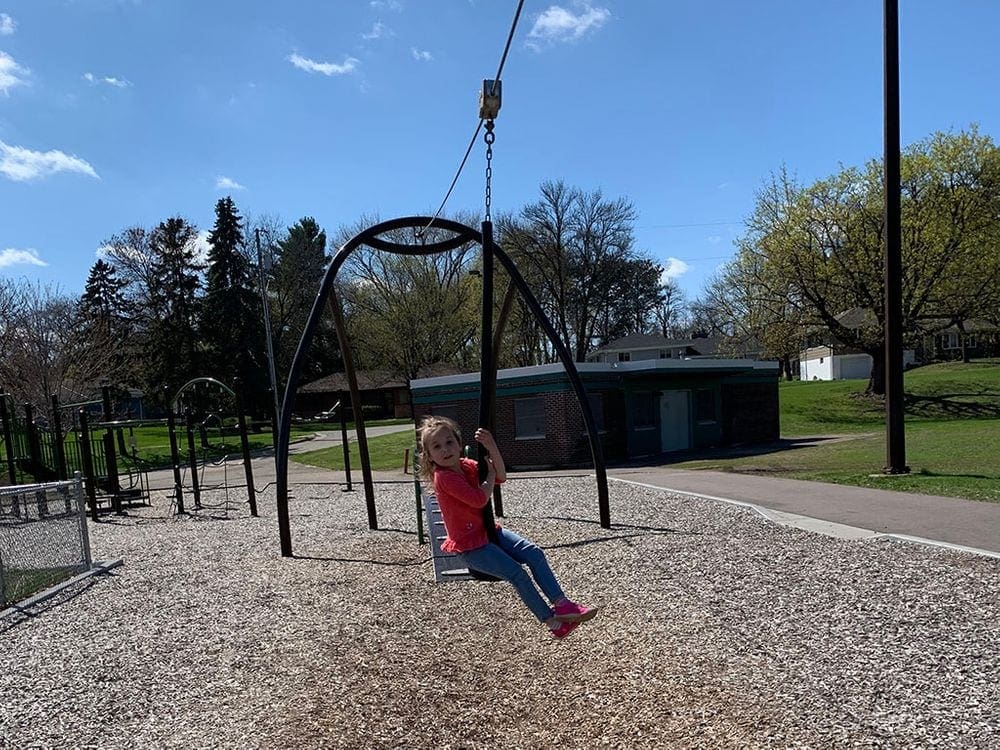 A young girl rides across a zipline at a playground, one of the best things to do in Minneapolis with kids.