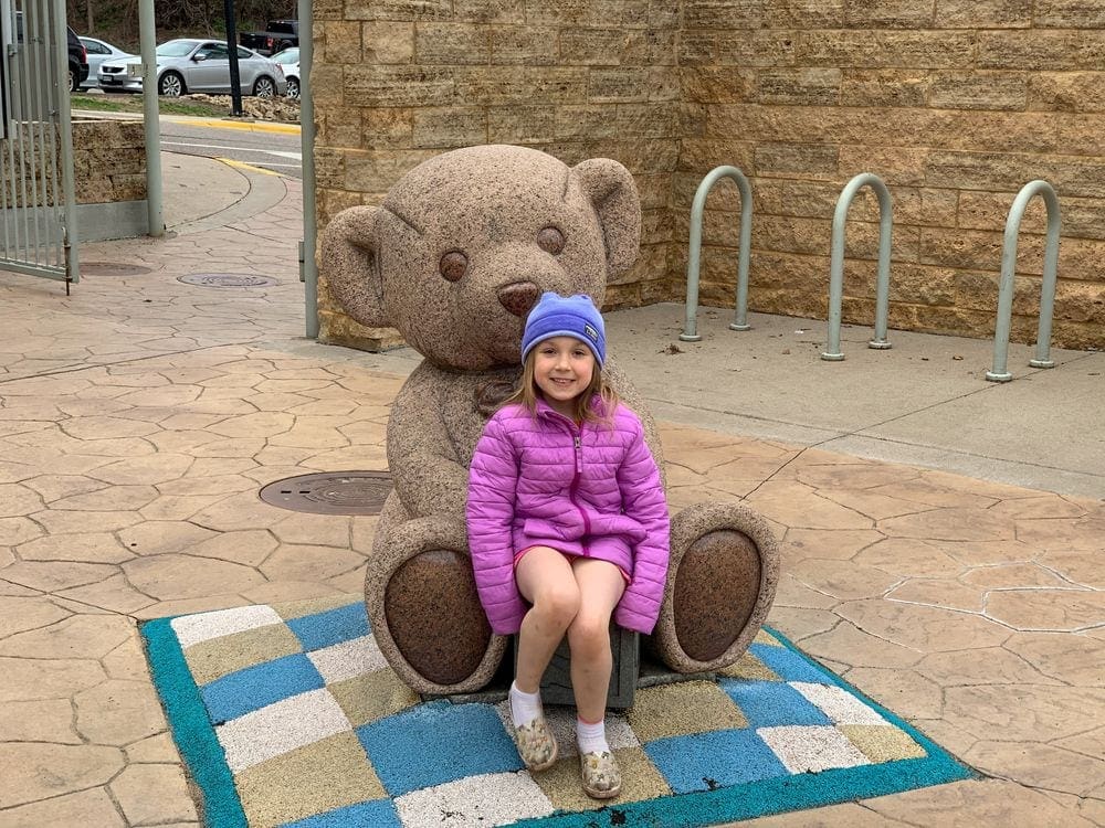 A young girl sits in the lap of a giant bear statue at the Teddy Bear Park in Stillwater, Minnesota.