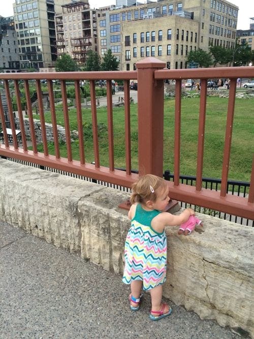 A young girl looks over the railing while walking alone Stone Arch Bridge in Minneapolis.