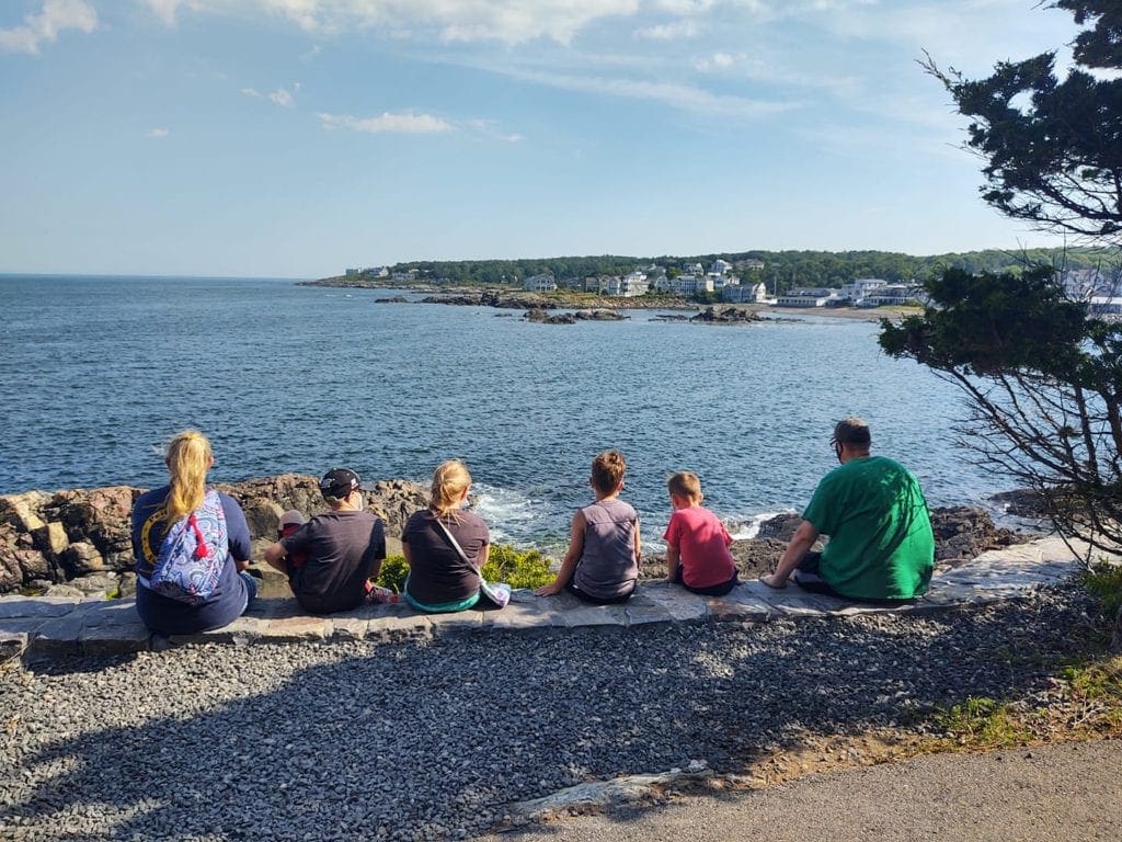 A family of six sits along the rocks facing the ocean from Ogunquit, one of the best places to visit in Maine with kids.