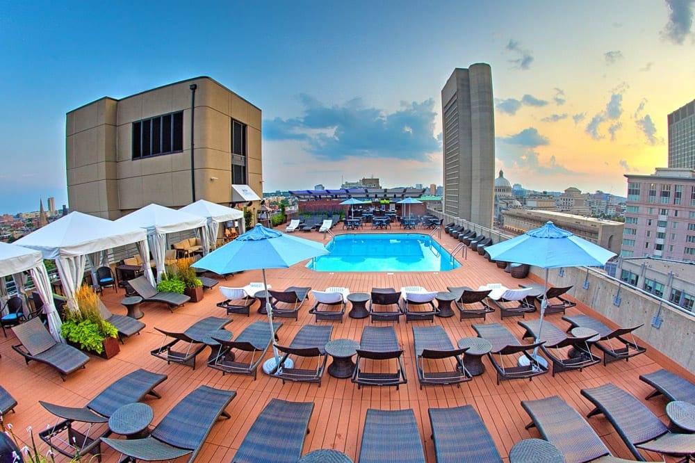 The rooftop pool at the The Colonnade Hotel on a sunny evening, with several loungers and umbrellas around the pool.