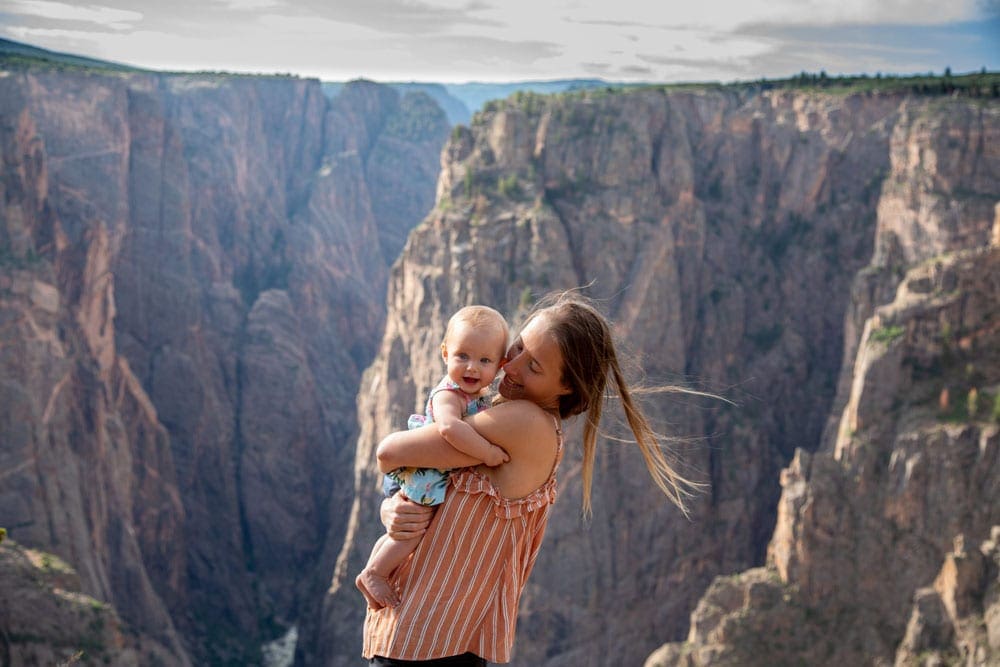 A mom snuggles her young baby with a canyon behind them.