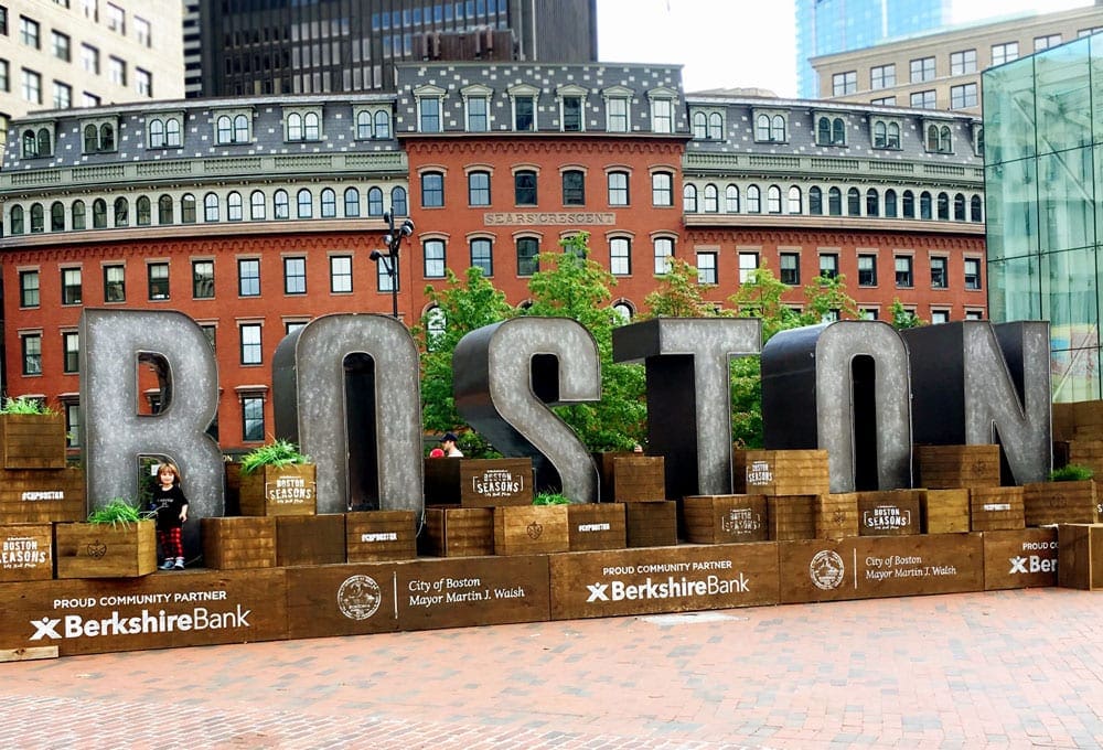A young child stands amongst a freestanding display spelling BOSTON.