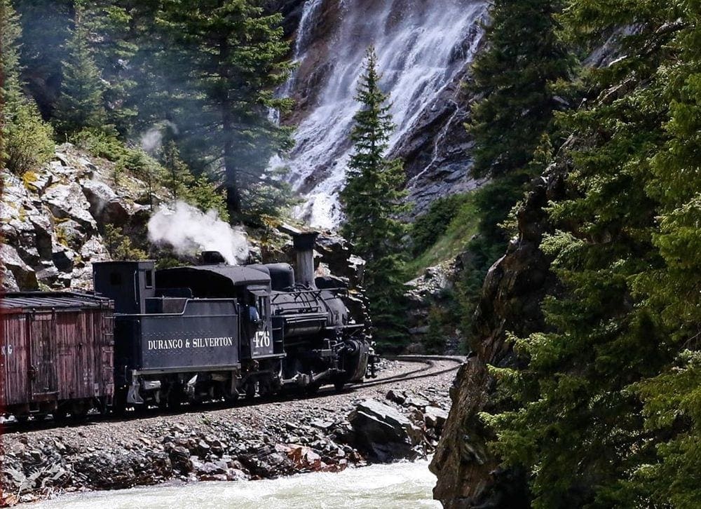 A black train rolls along the tracks in the beautiful Colorado scenery as part of a tour for Durango & Silverton Narrow Gauge Railroad, one of the best things to do in Colorado with kids.
