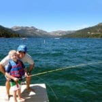 A boy holding a fishing pole smiles with his dad as they enjoy a beautiful day on Lake Tahoe.