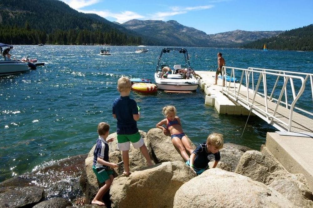 Four kids play in the nearby rocks while boats load and unload from a dock over Lake Tahoe.