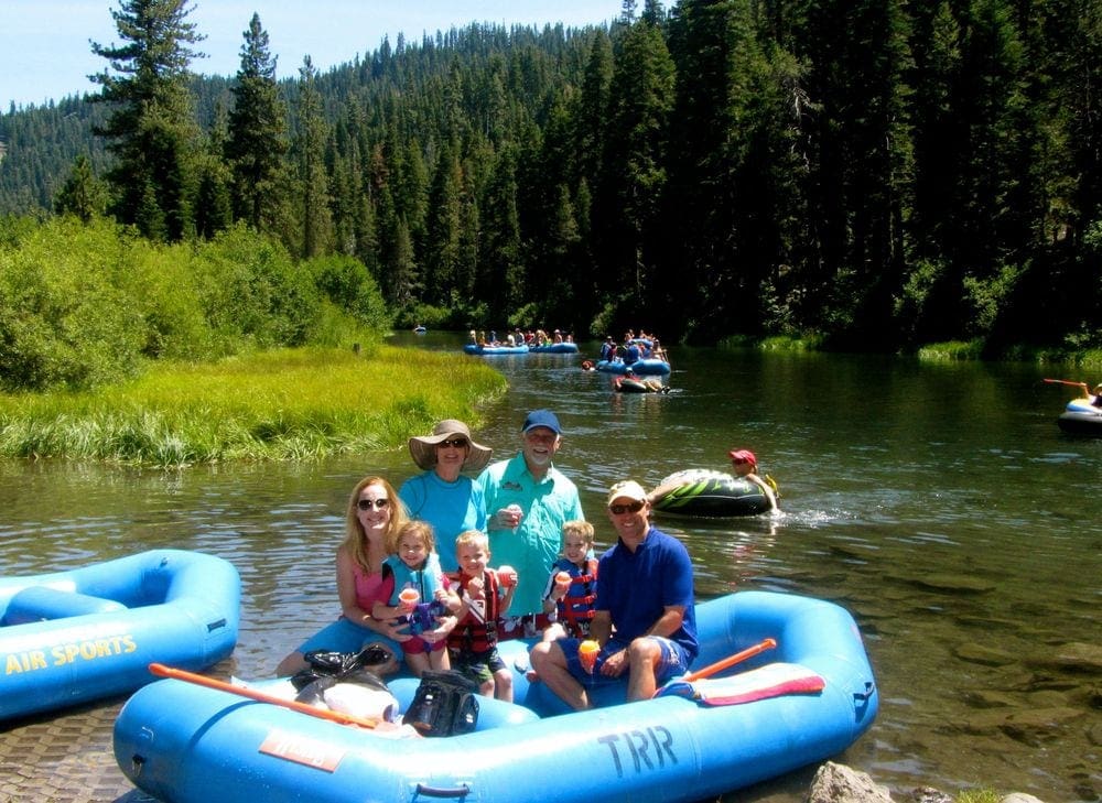 A family of 7, including grandparents, sits aboard a large blue raft along the Truckee River.