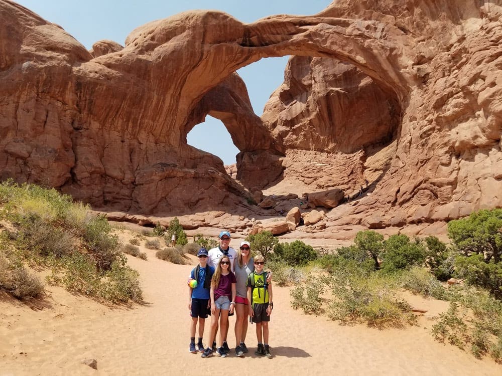 A family of five stands together posing in front of the iconic arches of Arches National Park near Moab, one of the best affordable summer vacations in the United States with kids.
