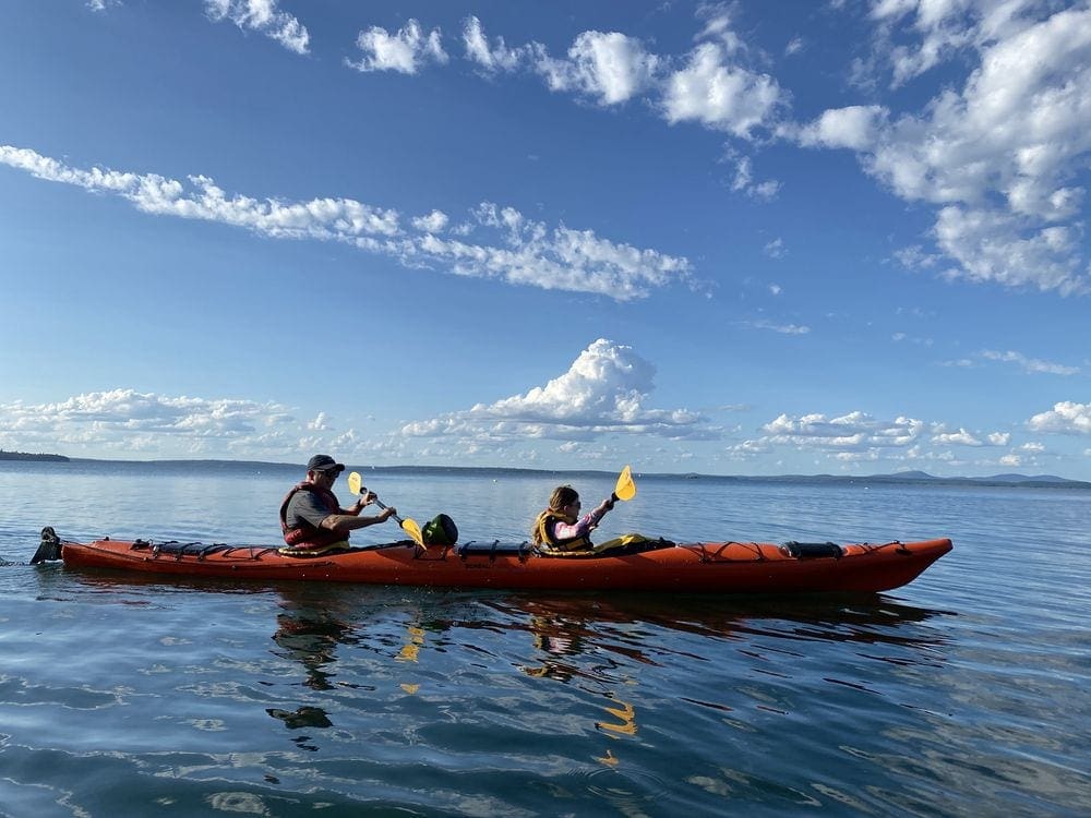 Two people paddle along in a tandem kayak while exploring the water off-shore from Bar Harbor, one of the best things to do in Bar Harbor with kids.
