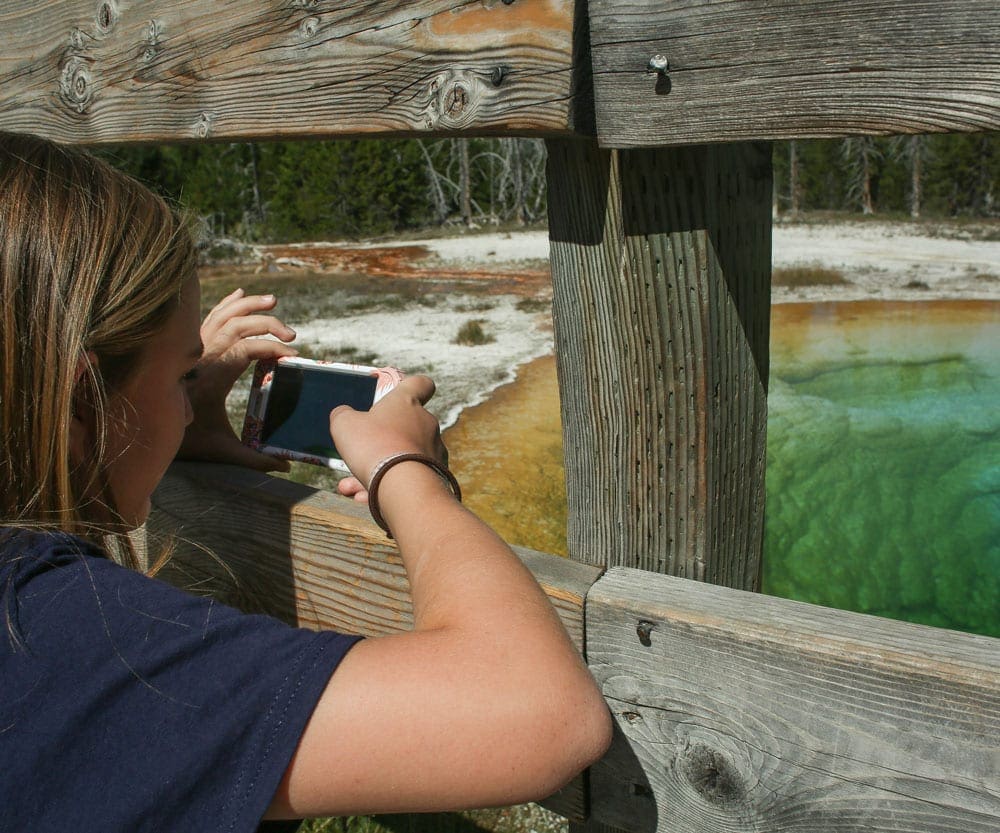 A young girl takes a picture through a fence of the Grand Prismatic at Yellowstone National Park.