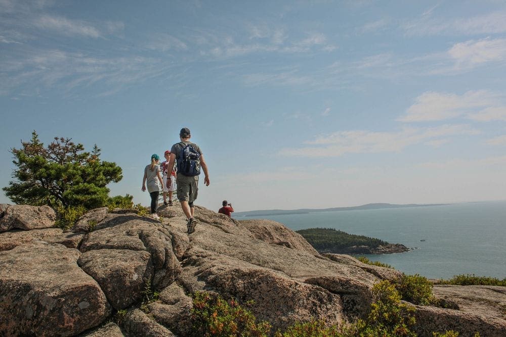 A family walks along the rocks atop a hike in Acadia National Park, one of the best things to do in Bar Harbor with kids.