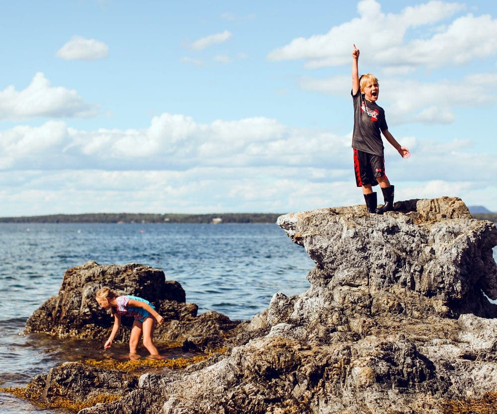 Two young children explore tide pools while explore Acadia National Park, one of the best affordable summer vacations in the United States with kids.