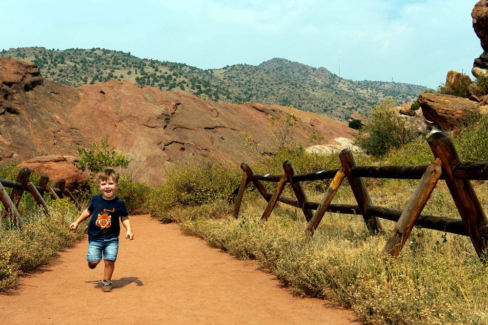 A young boy runs along a dusty path, while hiking in the Red Rocks of Colorado, a great stop on our one-week Colorado itinerary for families.