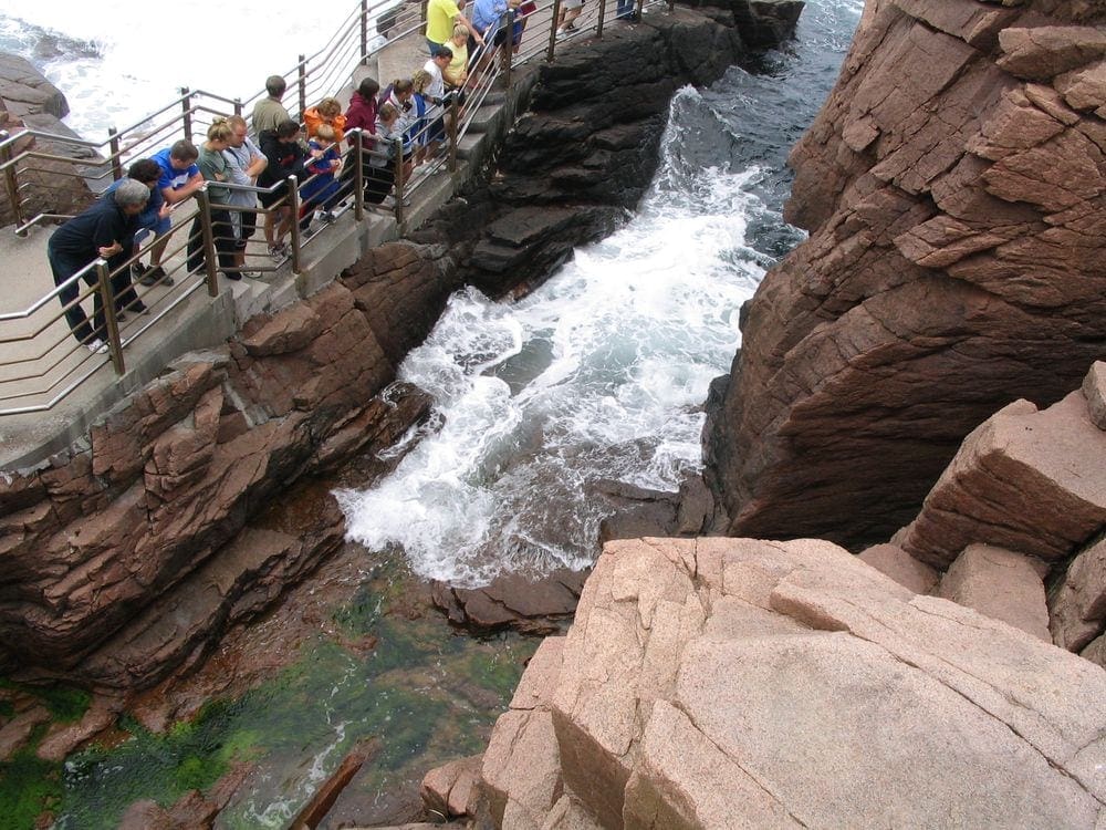 Several people lean over a railing to enjoy Thunder Hole, one of the best things to do in Bar Harbor with kids.