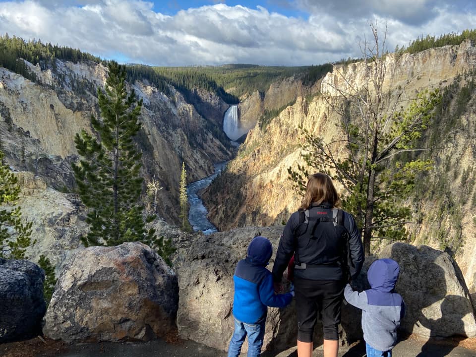 A mom stands with two kids while looking out onto a scenic view of Yellowstone National Park.