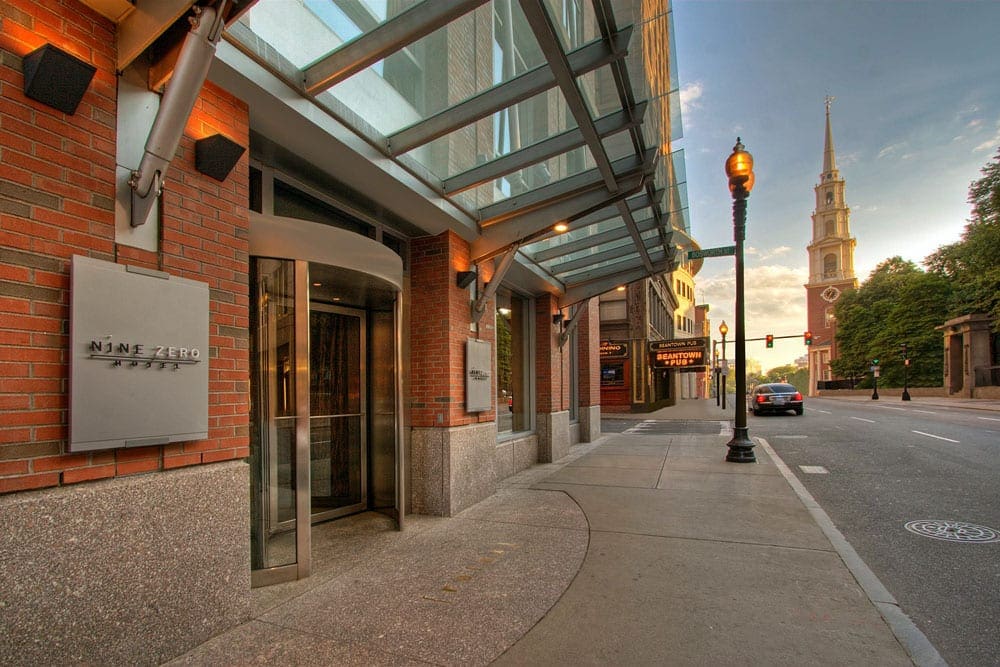 The entrance to the Kimpton Nine Zero Hotel at suset, one of the best hotels in boston for families, with historic buildings set on the adjacent corner.