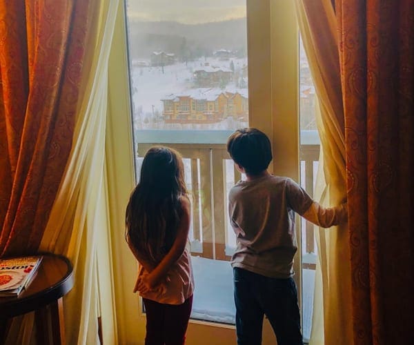Boy and a girl opening hotel curtains while staying at the Lodge at Spruce Peak, one of the best places to stay when skiing in Stowe with kids.