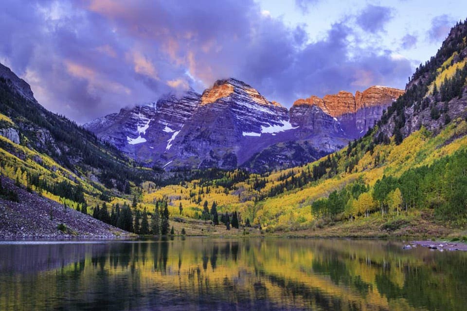 A stunning view of Maroon Bells, near Aspen, featuring a still lake and snow topped mountains.