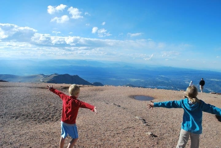 Two kids hold their arms out wide agains the wind at the top of Pikes Peak, one of the best things to do in Colorado with kids.