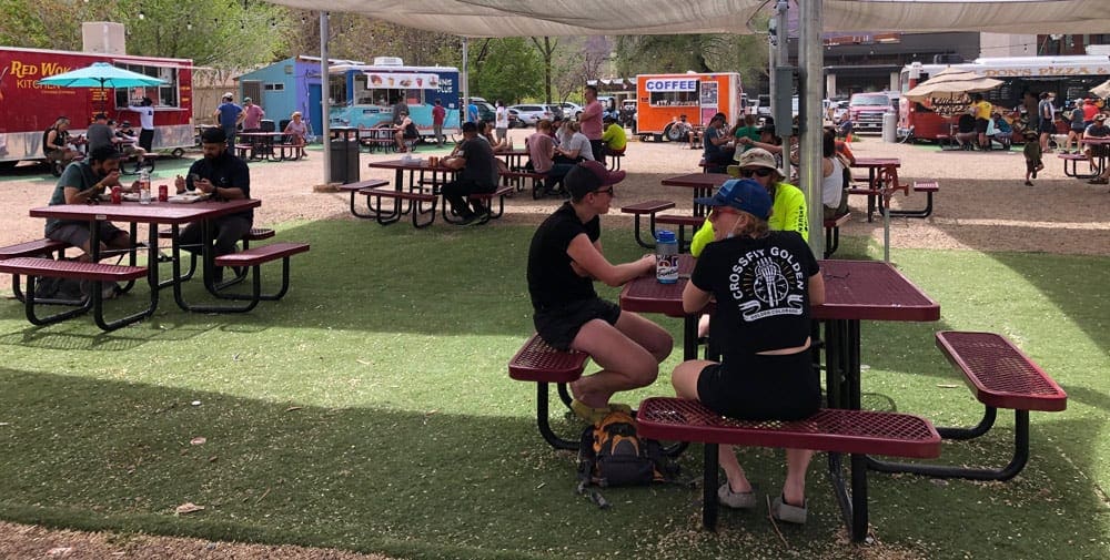 Several picnic tables host groups of people eating, with food trucks in the background at Moab Food Truck Park, one of the best things to do in Moab with kids.