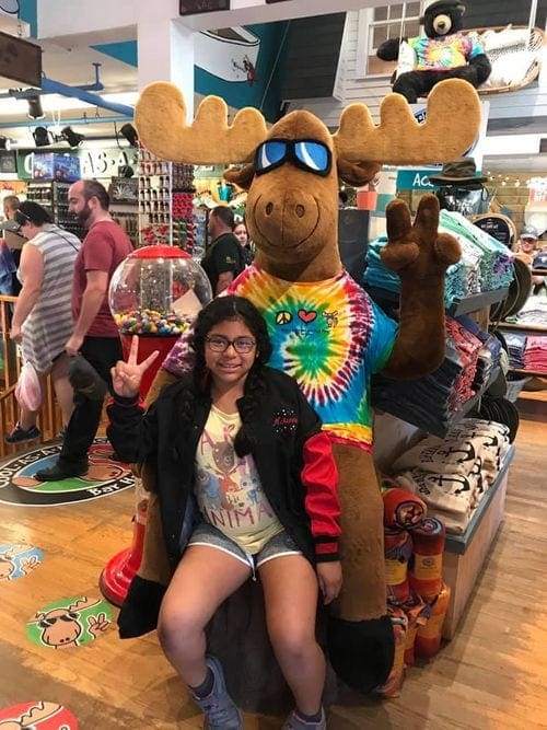 A young girl makes the peace sign while sitting on a large stuffed moose inside a shop while exploring downtown Bar Harbor.