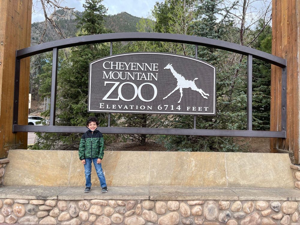 A young boy stands in front of the sign for the Cheyenne Mountain Zoo, a great stop on a our one-week Colorado itinerary for families.