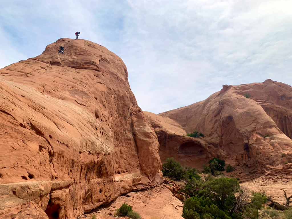 Two people climbing atop a large rock formation in Utah.