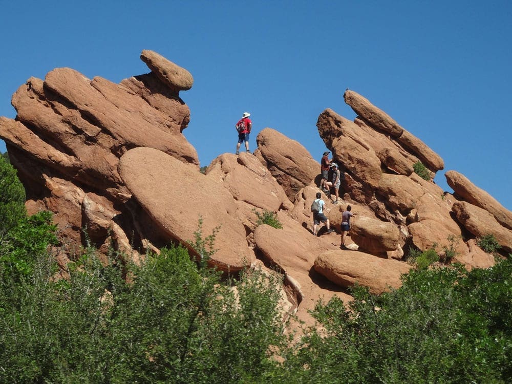 Three people climb amongst the huge bolders at the Garden of the Gods in Colorado, one of the best stops on our one-week Colorado itinerary for families.