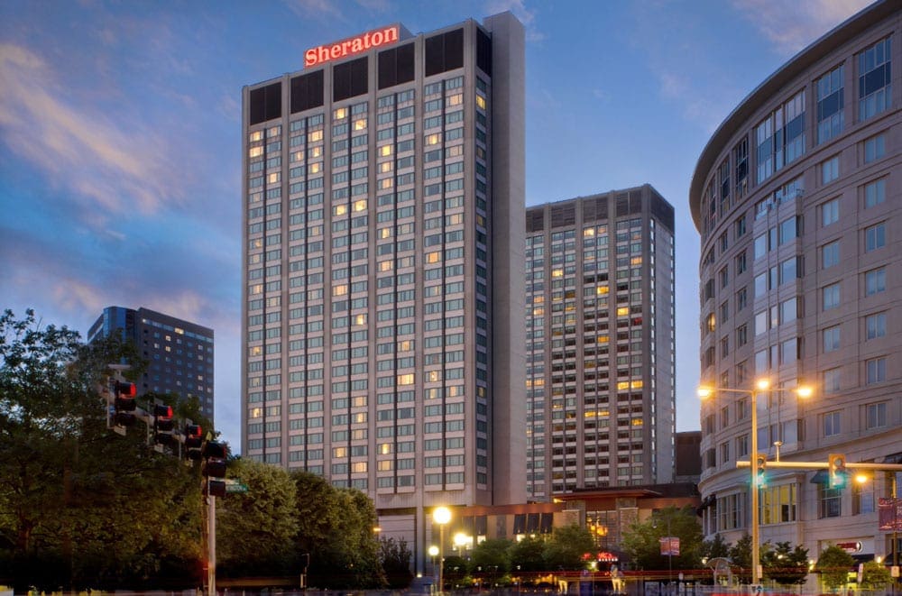 A view of the Sheraton Boston Hotel at night, brightly lit with the iconic red Sheraton sign on top.