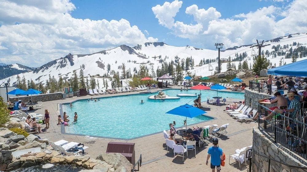 Several people enjoy a pool and the surrounding pool deck on a sunny day in Lake Tahoe.