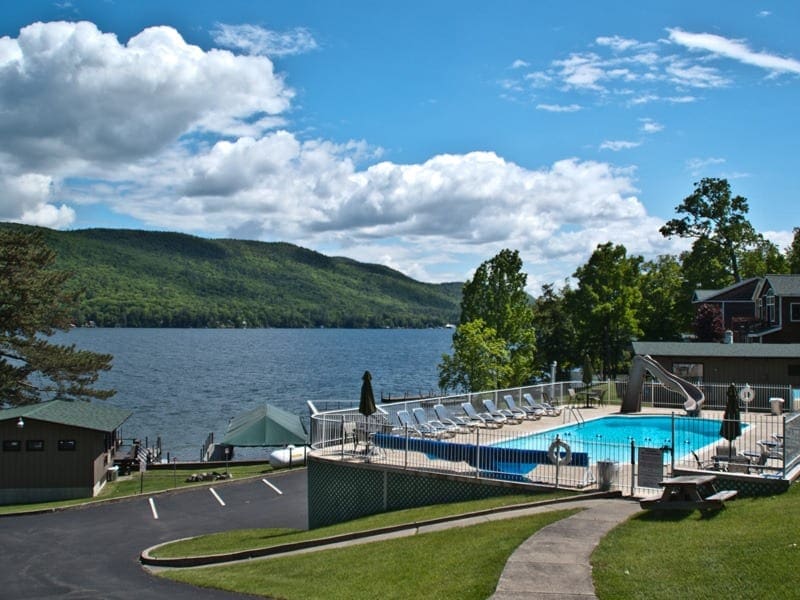 A sidewalk leads to the outdoor pool at Sun Castle Resort, one of the best family resorts in New York State, with the lake in the distance.