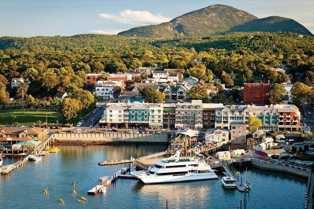 A view of West Street Hotel from the water, featuring pristine hotel grounds with marina access, with Maine's mountains in the distance.