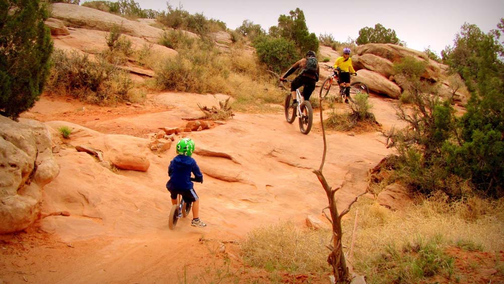 Three bikers peddle along a rocky path near Moab.