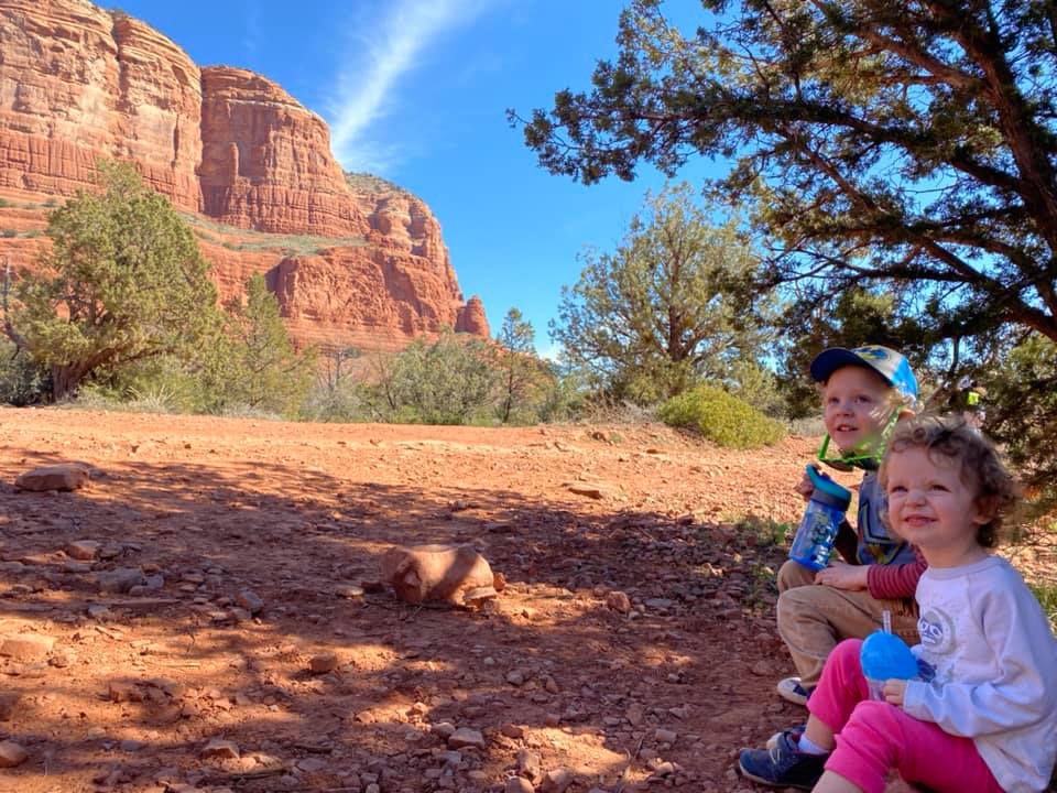 Two kids sit together in the shade, with Sedona's iconic red rocks in the distance.