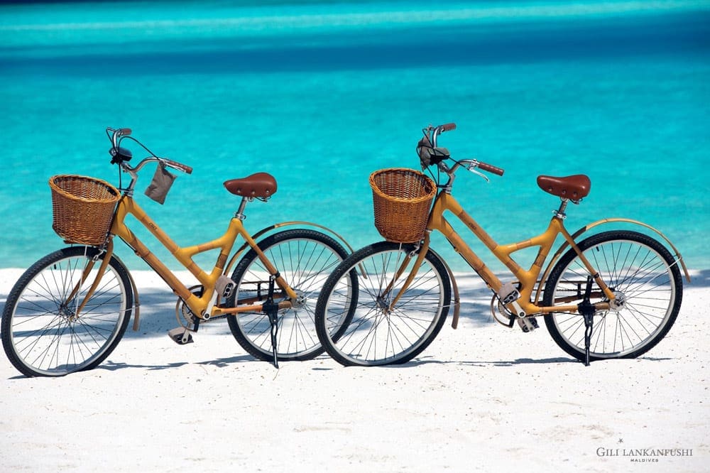 Two bikes with wicker baskets rest on the beach at the Gili Lankanfushi Maldives.