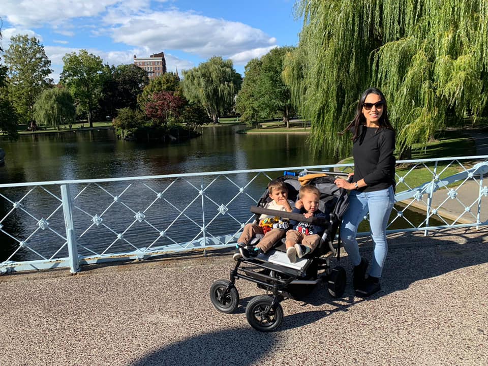 A mom pushes her two kids in a stroller while meanders a Boston park.