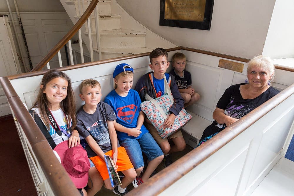 Six kids sit with their grandmother while resting at the Old North Church on their Freedom Trail Tour, one of the best things to do in Boston with kids.