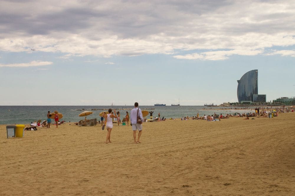 Several people dot Barceloneta Beach with buildings in the distance.