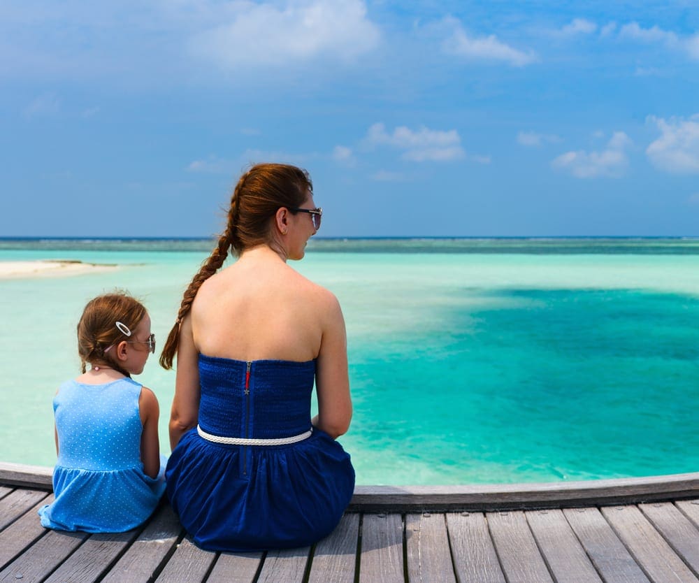 Mom and daughter sitting on a wooden dock looking at the beautiful ocean in the Maldives.